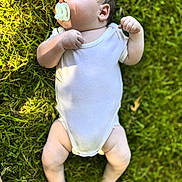 Colla is registered to the contest to win money with this photo: baby, barefoot, child, cute, grass, greenery, infant, lying_down, natural_light, outdoor, pacifier, peaceful, portrait, relaxation, skin, small, summer, sunlight, white_onesie, young