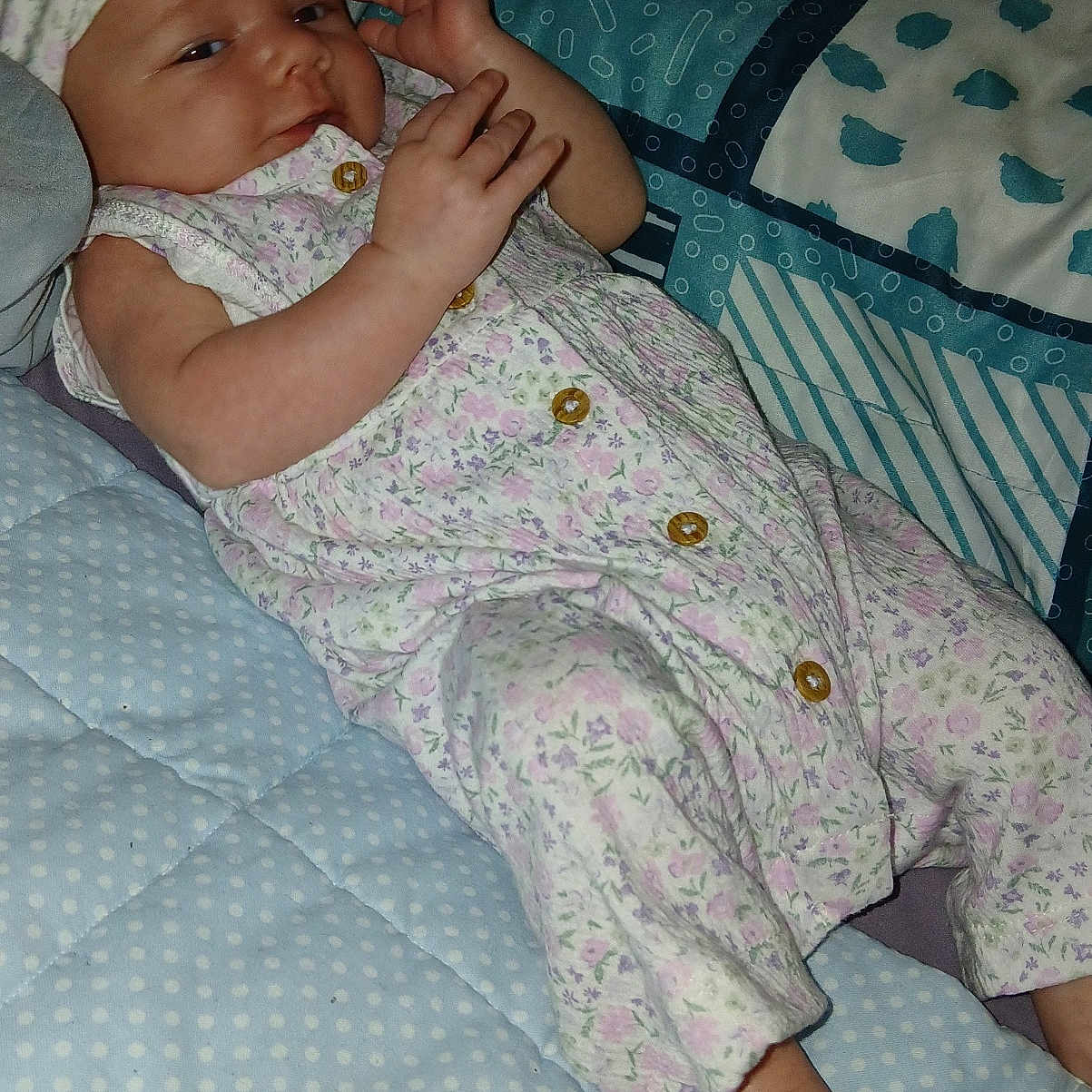 Aillanie is registered to the contest to win money with this photo: baby, bed, blanket, child, cute, floral, foot, hand, headband, indoor, infant, lying_down, onesie, pattern, person, portrait, quilt, resting, sleepwear, soft_lighting