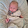 baby, infant, blanket, cushion, bed, face, person, newborn, sleepwear, cute, indoors, child, expression, portrait, soft_fabric, pattern, resting, small_hands, lying_down, cozy