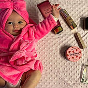 Romy participe au concours pour gagner de l'argent avec cette photo : baby, pink_robe, bow, blanket, beauty_products, cosmetics, face, infant, cute, smiling, lying_down, hand_up, soft_texture, skincare, perfume, makeup, child, portrait, indoors, playful