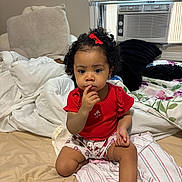 Amary is registered to the contest to win money with this photo: toddler, child, baby, red_shirt, bow, curly_hair, bed, blanket, pillow, window, air_conditioner, indoor, person, sitting, thinking, cute, home, cozy, young_child, portrait