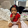 toddler, child, baby, red_shirt, bow, curly_hair, bed, blanket, pillow, window, air_conditioner, indoor, person, sitting, thinking, cute, home, cozy, young_child, portrait