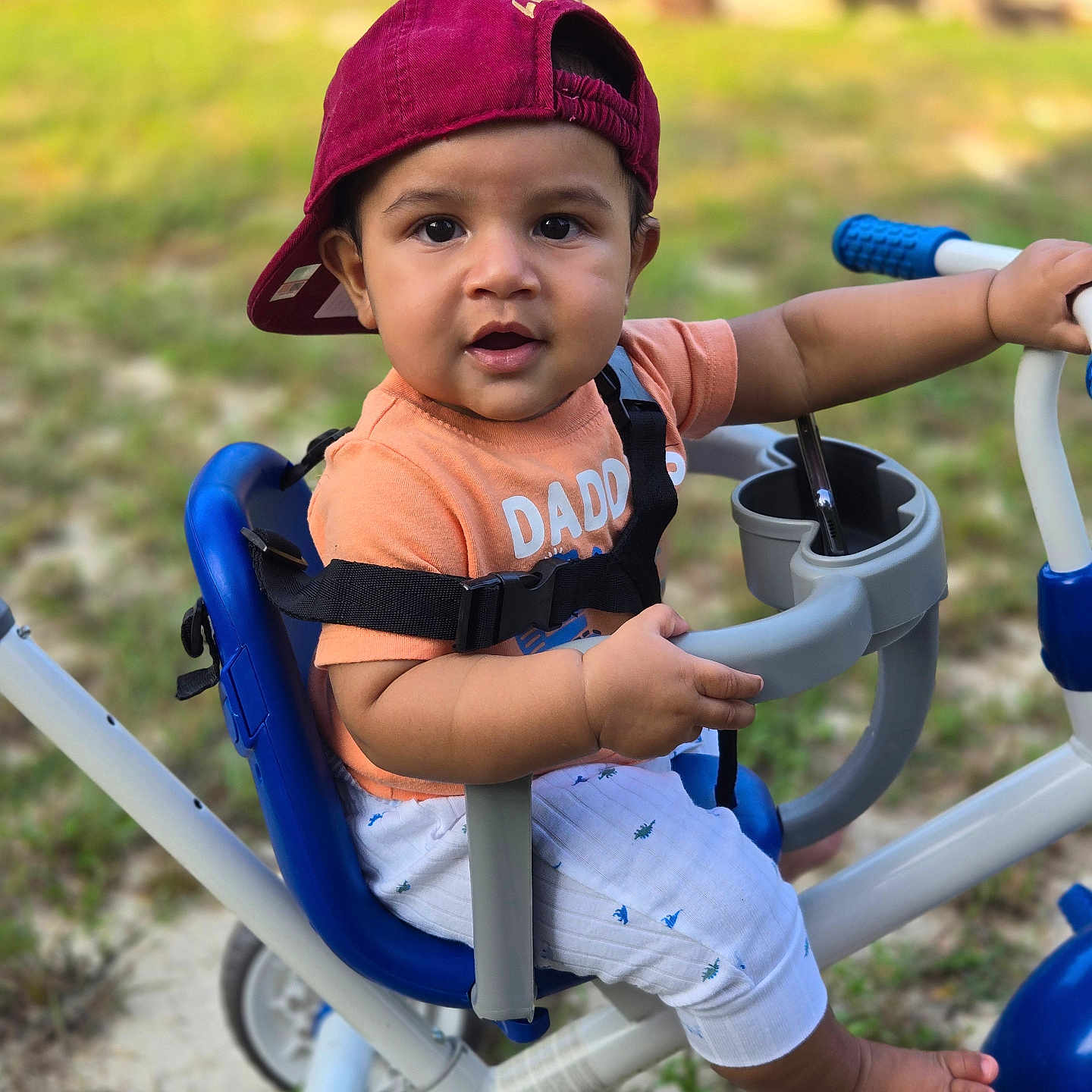 Carter is registered to the contest to win money with this photo: baby, baseballcap, bodypart, cap, clothing, face, finger, glove, grass, hand, hat, head, machine, outdoors, person, photography, portrait, transportation, vehicle, wheel