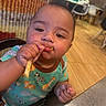 Brayan joined the competition — help win amazing prizes! baby, child, french_fries, food, high_chair, indoor, restaurant, table, chair, clothing, animal_print, eating, face, hand, cute, young_child, person, skin, expression, closeup