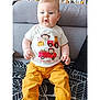 baby, blanket, blue_eyes, child, couch, crib, cute, face, furniture, home, indoor, infant, light_hair, portrait, seated, smiling, socks, toy, tshirt, yellow_pants