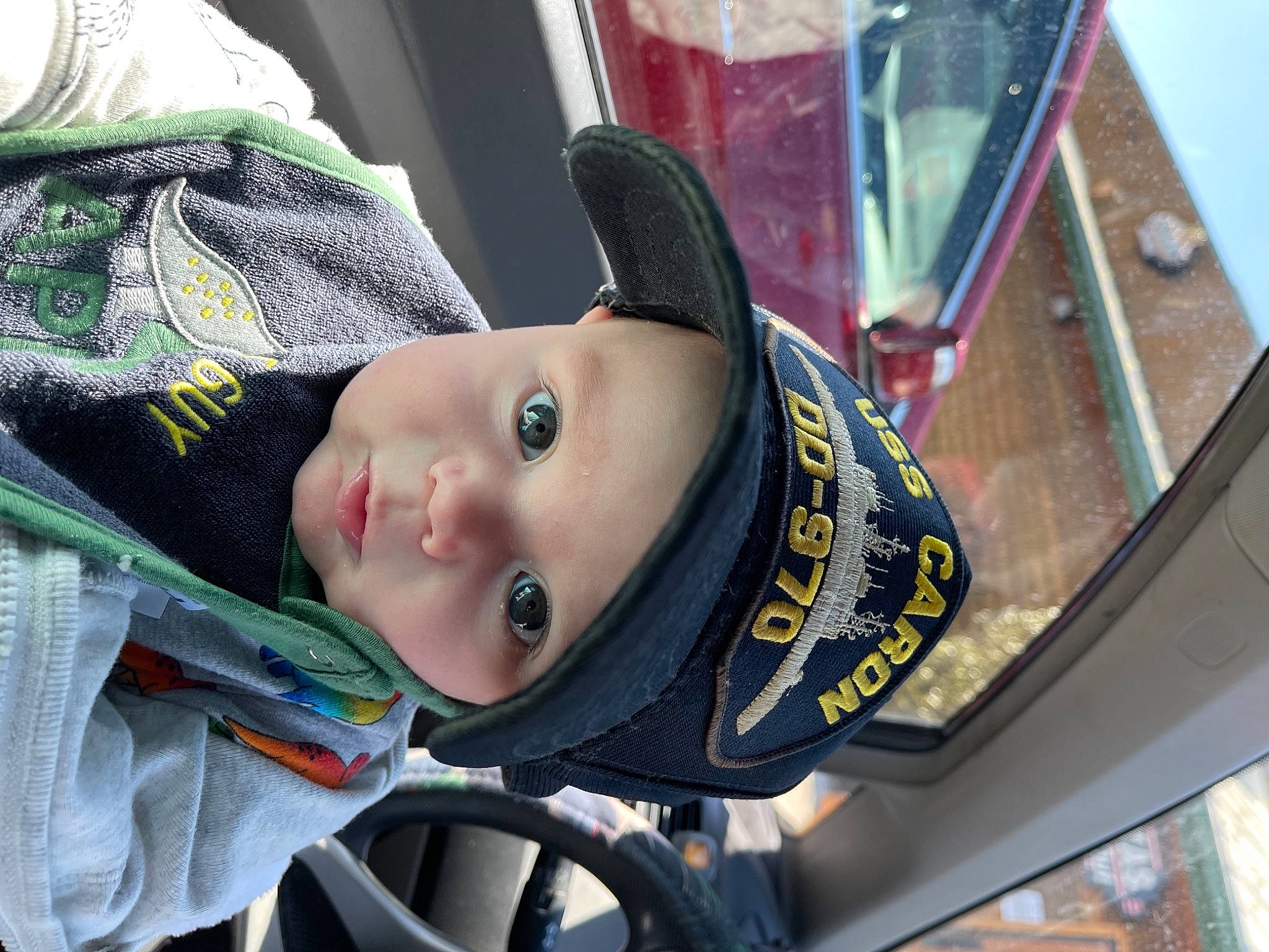 Branson is registered to the contest to win money with this photo: auto_part, baby, baby_carriage, baby_products, car_seat, cheek, child, eye, fun, headgear, headwear, helmet, motor_vehicle, person, personal_protective_equipment, smile, street_fashion, toddler, tree, vehicle