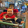 Bowen is registered to the contest to win money with this photo: baby, shopping_cart, indoor, store, child, smiling, clothing, red, blue, decorations, fish, retail, floor, person, happy, seat, shopping, aisle, furniture, light