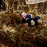 baby, dog, couch, floral_pattern, vintage, wood_paneling, blanket, indoors, pet, child, relaxing, animal, furniture, carpet, cozy, portrait, living_room, canine, comfort, casual