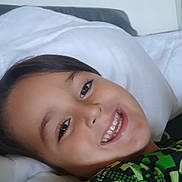 Giulian a rejoint le concours — aidez-le/la à gagner de superbes lots ! bed, casual, child, clothing, eyes, face, green_shirt, hair, happy, home, indoors, mouth, person, pillow, portrait, resting, skin, smiling, white_bedding, young