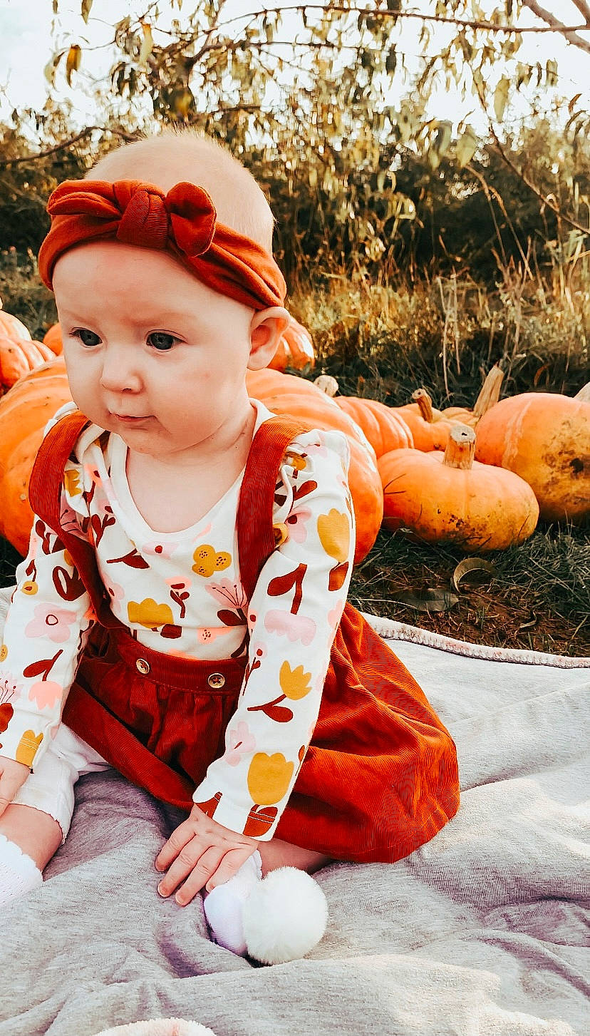 Esmae joined the competition — help win amazing prizes! baby, baby_toddler_clothing, calabaza, cap, child, clothing, dress, eye, face, gourd, grass, happy, headwear, orange, pattern, peach, people_in_nature, person, plant, sitting