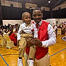 Jamie Cosley joined the competition — help win amazing prizes! man, child, toddler, formal_wear, red_vest, bow_tie, suspenders, white_shirt, beige_pants, indoor, event, people, seated, gymnasium, wood_floor, smile, family, celebration, group, portrait