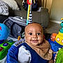 baby, child, smile, face, indoor, toy, activity_center, globe_toy, submarine_toy, bib, clothing, furniture, couch, blanket, floor, person, head, happy, infant, playtime