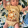 baby, infant, child, portrait, lying_down, blanket, colorful_blanket, onesie, duck_design, flower_design, serious_expression, raised_arms, hands, legs, indoor, close_up, face, baby_clothing, text_on_clothing, cozy