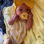 Kemberly is registered to the contest to win money with this photo: baby, infant, child, portrait, lying_down, pacifier, headband, bow, yellow, blanket, onesie, sun_pattern, sleeping_area, closeup, face, hands, arms, legs, indoor, cozy