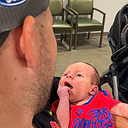 Aaron Jr joined the competition — help win amazing prizes! baby, newborn, child, infant, person, face, portrait, sitting, being_held, red_clothing, basketball_jersey, sportswear, clippers, stroller, chairs, waiting_room, indoor, adult, father, smiling