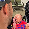 baby, newborn, child, infant, person, face, portrait, sitting, being_held, red_clothing, basketball_jersey, sportswear, clippers, stroller, chairs, waiting_room, indoor, adult, father, smiling
