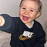 Thélyo participe au concours pour gagner de l'argent avec cette photo : bed, black_clothing, blanket, child, clean_background, eyes, face, hand, happy, indoors, infant, laughing, nike, playful, portrait, reaching, smiling, sweatshirt, teeth, toddler