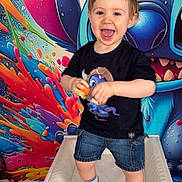Thélyo a rejoint le concours — aidez-le/la à gagner de superbes lots ! child, toddler, smiling, standing, toy, sneakers, denim_shorts, tshirt, colorful_background, wall_art, cartoon_character, portrait, happy, indoor, playful, cheerful, face, hands, eyes, mouth