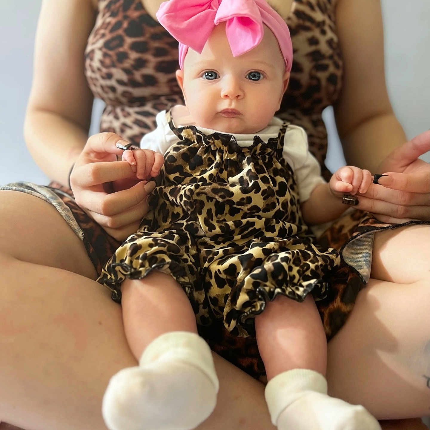 Klara Mae is registered to the contest to win money with this photo: baby, child, infant, portrait, sitting, pink_bow, leopard_print, dress, white_socks, adult, parent, hands, fashion, indoors, close_up, face, eyes, cute, family, photography