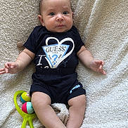 Andréas a rejoint le concours — aidez-le/la à gagner de superbes lots ! baby, beige_blanket, black_clothing, blanket, child, comfortable, crossed_feet, curious_expression, cute, green_toy, guess_logo, indoor, infant, lying_down, person, playful, rattle_toy, soft_texture, toddler, wide_eyes