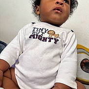 Vontarius joined the competition — help win amazing prizes! baby, child, curly_hair, white_shirt, text_on_clothing, lion_graphic, plush_toy, eye_graphic, indoor, soft_lighting, cute, innocence, curiosity, portrait, seated, close_up, hand, skin, face, clothing