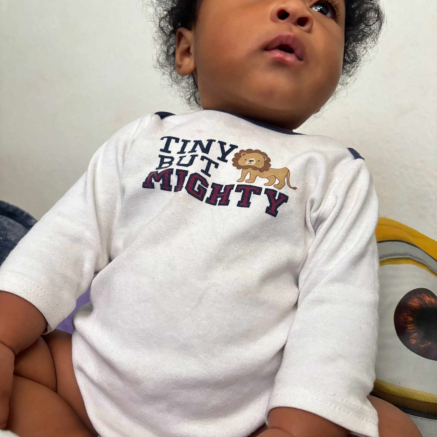 Vontarius joined the competition — help win amazing prizes! baby, child, curly_hair, white_shirt, text_on_clothing, lion_graphic, plush_toy, eye_graphic, indoor, soft_lighting, cute, innocence, curiosity, portrait, seated, close_up, hand, skin, face, clothing