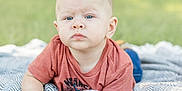 Kaysen is registered to the contest to win money with this photo: baby, blanket, blue_eyes, child, closeup, cute, daytime, grass, head, infant, laying_down, nature, outdoor, person, portrait, red_shirt, serious_expression, skin, soft_light, young_child