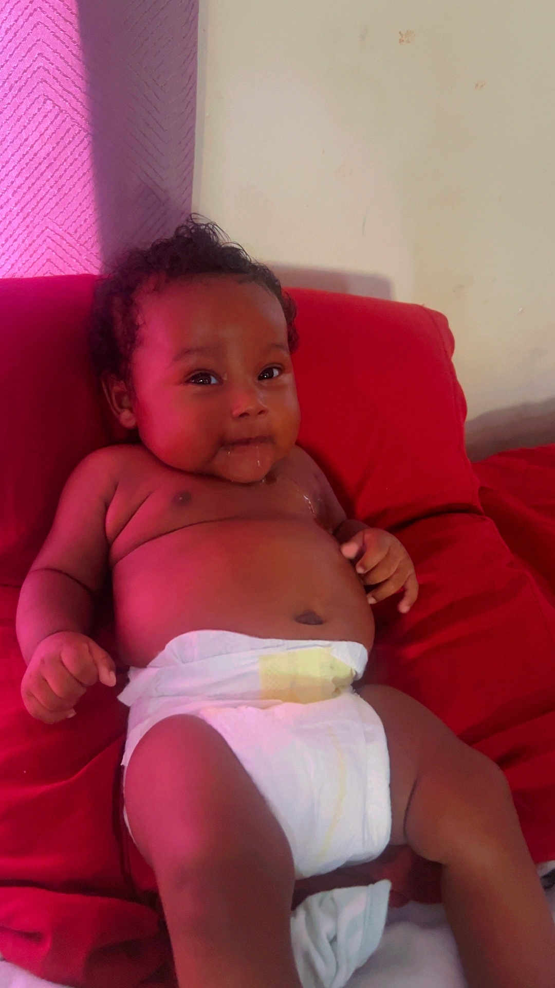Ahki is registered to the contest to win money with this photo: baby, diaper, infant, cushion, red, drool, cute, skin, chubby, relaxing, indoors, child, smiling, person, portrait, curly_hair, lying_down, plush, comfort, young