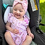 baby, infant, smiling, headband, bow, pink_dress, car_seat, pacifier, toy, outdoor, grass, skin, legs, feet, socks, portrait, happy, cute, accessory, seatbelt_warning