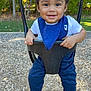 toddler, child, swing, playground, smiling, curly_hair, blue_bib, white_shirt, blue_pants, socks, outdoor, trees, autumn, woodchips, daylight, happy, person, park, nature, play
