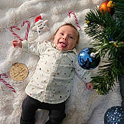 Théo a rejoint le concours — aidez-le/la à gagner de superbes lots ! baby, bauble, blanket, candy_cane, christmas_ornament, christmas_tree, clothing, cute, decorations, festive, happy, holiday, indoors, infant, pants, person, smiling, socks, tongue_out, white_blanket