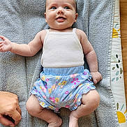 Anna participe au concours pour gagner de l'argent avec cette photo : baby, smiling, infant, clothing, tank_top, shorts, floral_pattern, towel, hand, skin, foot, lying_down, happy, cute, indoors, person, child, playful, floor, texture
