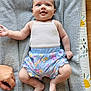 baby, smiling, infant, clothing, tank_top, shorts, floral_pattern, towel, hand, skin, foot, lying_down, happy, cute, indoors, person, child, playful, floor, texture