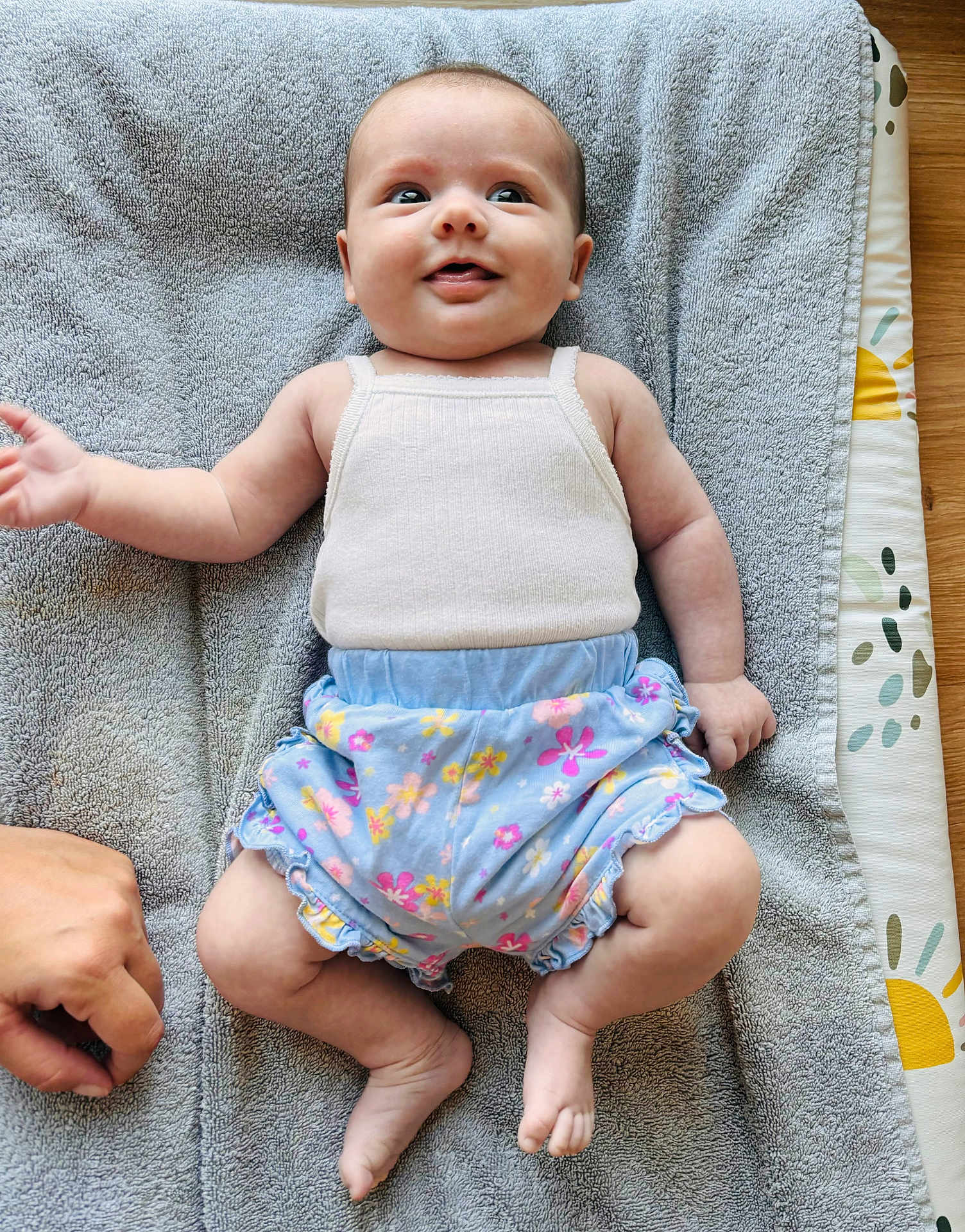 Anna participe au concours pour gagner de l'argent avec cette photo : baby, smiling, infant, clothing, tank_top, shorts, floral_pattern, towel, hand, skin, foot, lying_down, happy, cute, indoors, person, child, playful, floor, texture