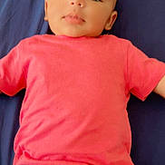 Muhammad Ali is registered to the contest to win money with this photo: baby, child, infant, portrait, face, clothing, pink_shirt, dark_pants, lying_down, blue_background, skin, head, eyes, mouth, ear, young, person, indoors, casual, calm