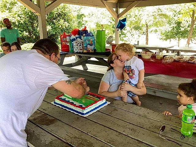 Joseph is registered to the contest to win money with this photo: child, event, flooring, fun, leisure, party, person, play, public_space, recreation, shade, sharing, shorts, sitting, social_group, summer, t_shirt, table, toddler, tree