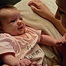 Rosalie is registered to the contest to win money with this photo: baby, infant, child, sibling, family, smiling, happy, portrait, close_up, lying_down, bed, bedding, indoors, warm_lighting, pink_clothing, romper, bare_feet, face, cuddling, candid