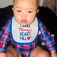 Antonio is registered to the contest to win money with this photo: baby, child, infant, plaid_shirt, bib, sitting, cute, portrait, indoor, person, young_child, face, hand, legs, hair, clothing, expression, curious, red_heart, small_ponytail