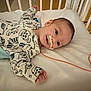 baby, infant, crib, onesie, dinosaur_pattern, medical_tube, tape, lying_down, bed, blanket, indoors, child, cute, person, face, head, expression, healthcare, pediatric, hospital