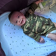 Rivver is registered to the contest to win money with this photo: baby, infant, child, smiling, camouflage, onesie, bassinet, crib, blanket, bottle, nursery, sleeping_area, star_pattern, moon_pattern, lying_down, portrait, happy, indoor, face, infant_bed