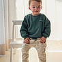 toddler, child, smiling, standing, sweater, striped_pants, socks, indoor, curtain, step_stool, light, shadow, floor, home, person, young_child, cute, portrait, casual, happy