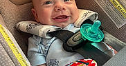 Carter is registered to the contest to win money with this photo: baby, infant, car_seat, smile, pacifier, toy, straps, clothing, face, child, seatbelt, happy, indoors, closeup, cute, person, head, sitting, safety, car