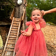 Isla is registered to the contest to win money with this photo: toddler, child, dress, pink, smile, hand_holding, outdoor, tree, wooden_ladder, nature, happy, person, young_child, playful, sunlight, greenery, portrait, cute, daylight, fashion