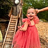 toddler, child, dress, pink, smile, hand_holding, outdoor, tree, wooden_ladder, nature, happy, person, young_child, playful, sunlight, greenery, portrait, cute, daylight, fashion