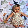 baby, smile, child, dress, headband, cupcake, candle, butterfly, blanket, sitting, happy, celebration, flower_pattern, cute, portrait, infant, birthday, colorful, indoors, young_child
