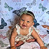 baby, child, smile, headband, dress, butterfly, blanket, pattern, cute, happy, infant, portrait, sitting, skin, hand, foot, blue_eyes, person, indoors, colorful