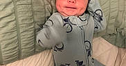 River joined the competition — help win amazing prizes! baby, bed, bicycle_pattern, blanket, blue_clothing, child, cute, face, happy, head, home, indoor, infant, lying_down, onesie, person, quilt, sleepwear, smile, soft_lighting