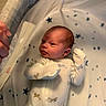 newborn, baby, infant, onesie, crib, bassinet, star_pattern, hand, netting, sleepwear, cute, young_child, indoor, soft_lighting, resting, clothing, face, person, baby_sleeping, baby_bed
