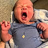 newborn, baby, yawning, blue_onesie, blanket, infant, cute, sleepy, small_hand, tattooed_arm, soft_texture, indoor, person, portrait, face, expression, clothing, human, wrapped, cozy