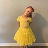 child, girl, yellow_dress, bow, posing, indoor, floor, wall, portrait, smile, long_hair, fashion, clothing, footwear, black_shoes, cute, standing, young, happy, casual